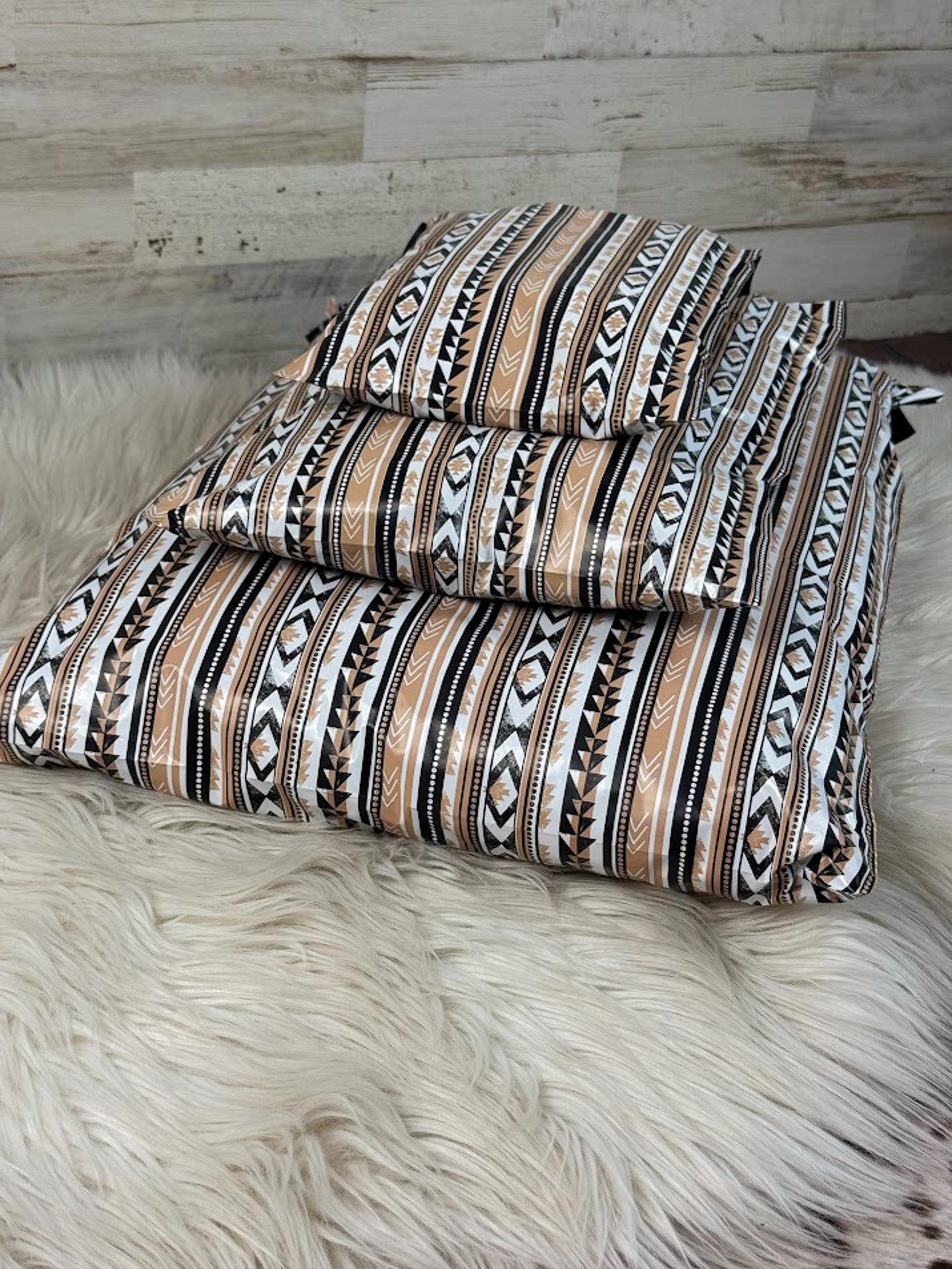 A poly mailer set with a Southwestern geometric pattern in beige, brown, black, and white, displayed on a white faux fur rug against a rustic wood plank wall.
