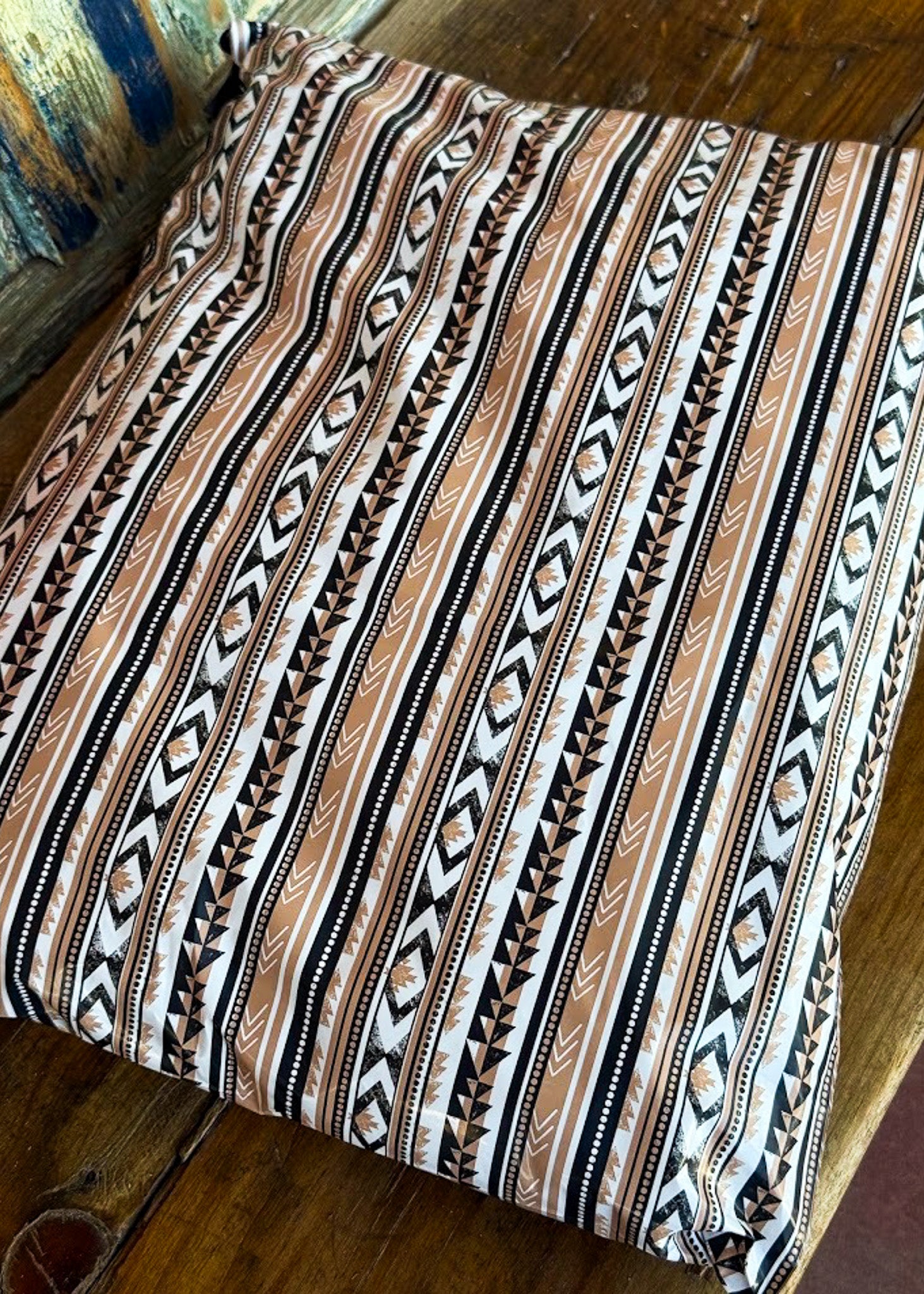 A poly mailer with a brown, black, and white Southwestern geometric pattern, resting on a rustic wooden surface.