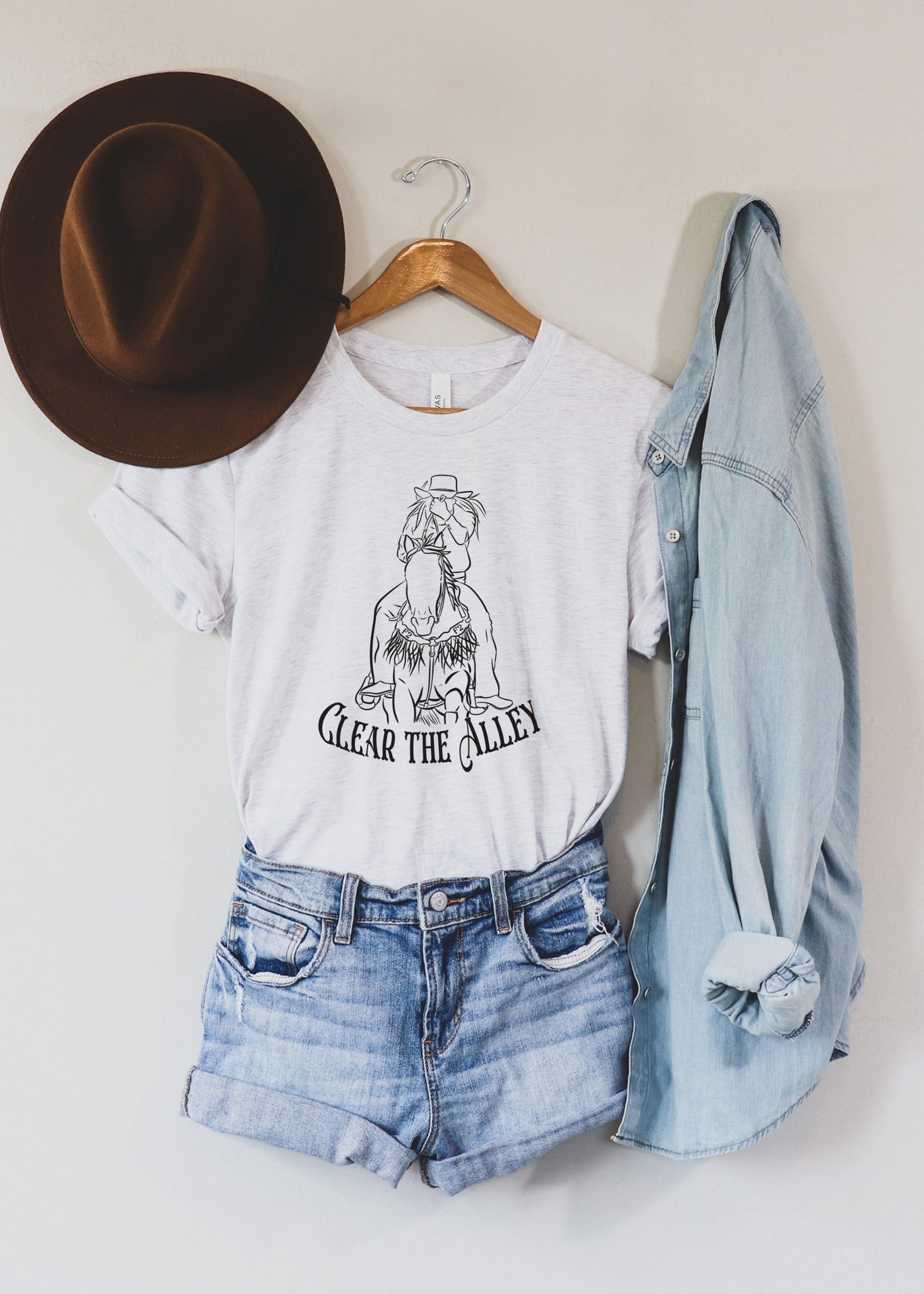 clear the alley rodeo barrel racer graphic tee on ash shirt, hanging on wall paired with denim shirt, shorts and hat