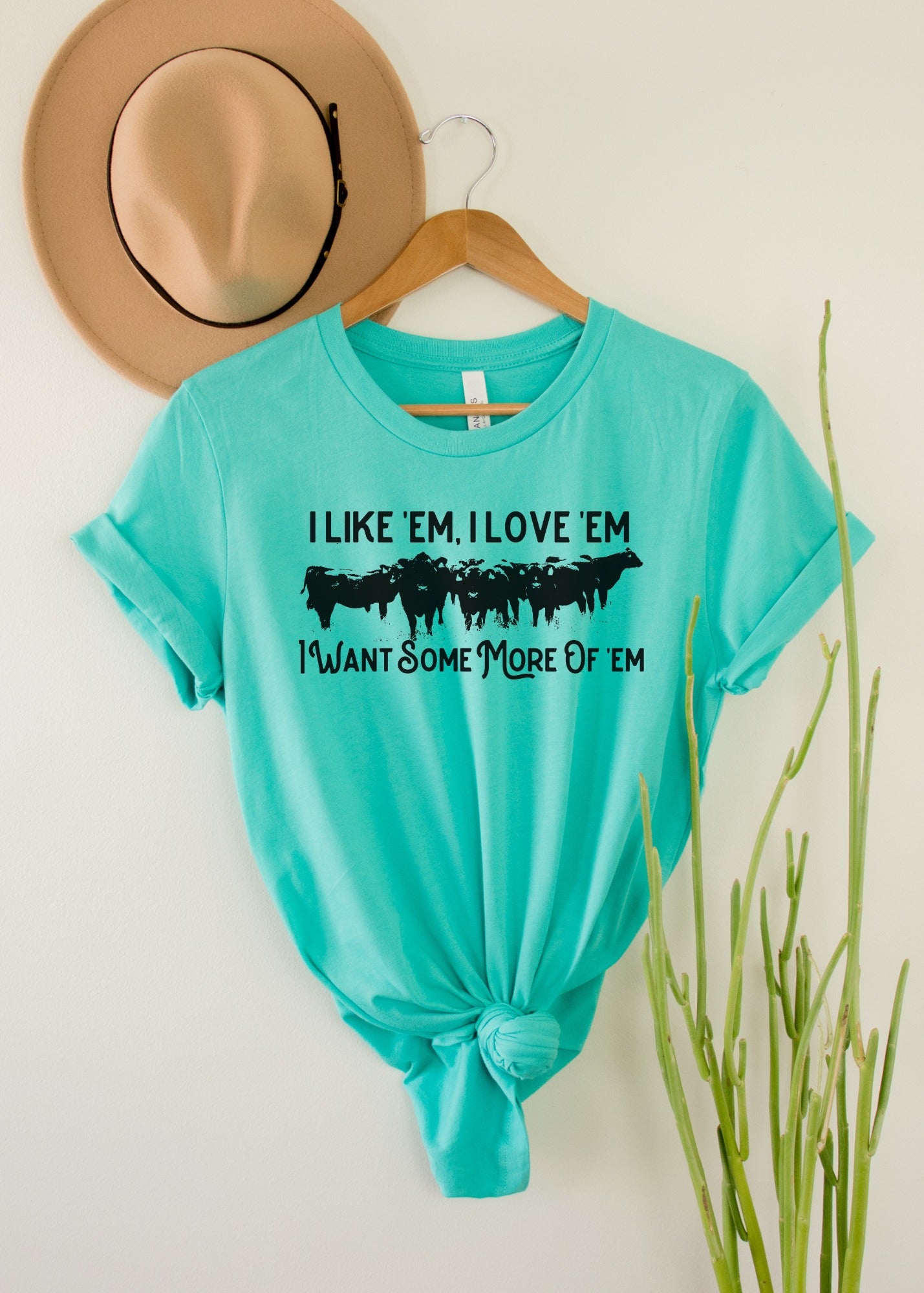 teal wholesale western graphic tee with cow herd print hanging on wood background with cactus decor