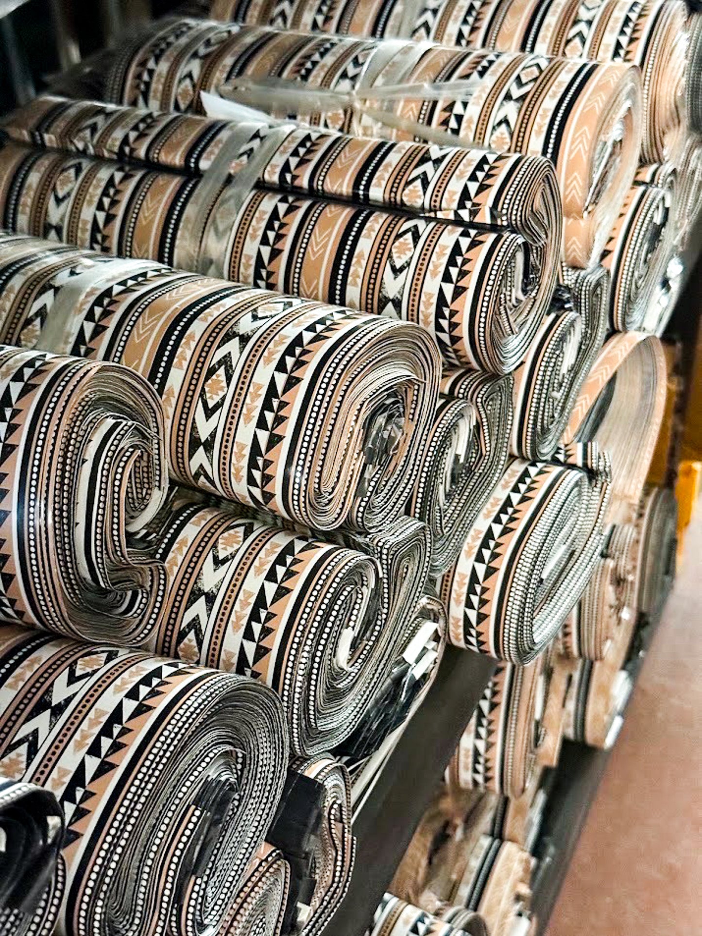 Stacks of rolled poly mailers with geometric tribal patterns in beige, black, and brown, displayed on a rack.
