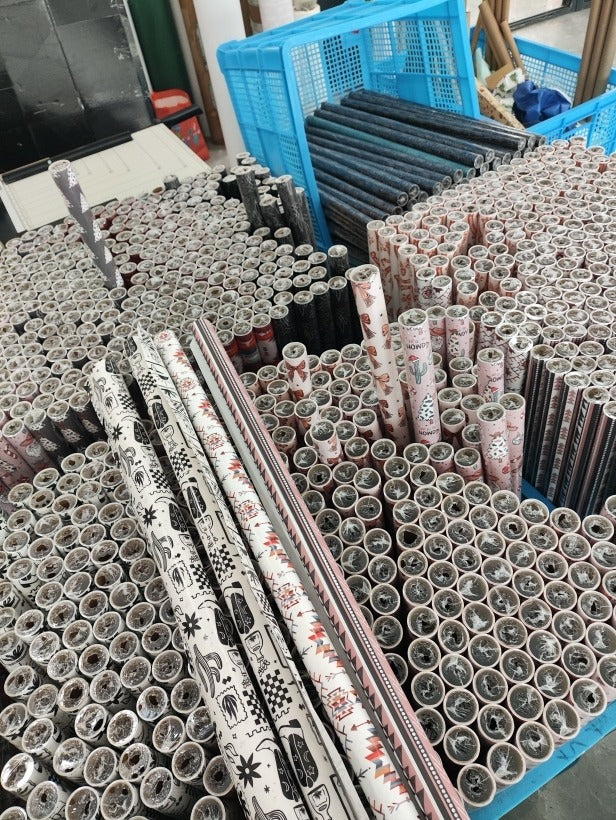A large bulk display of rolled wrapping paper and gift boxes stacked on blue plastic pallets in a warehouse or storage area.